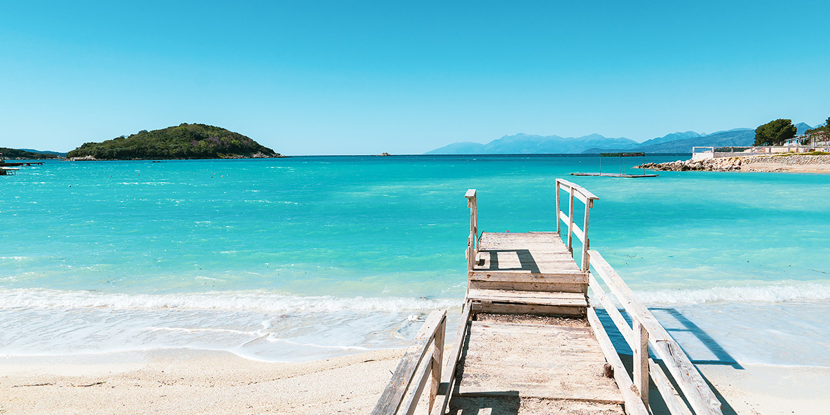 Kritthvit strand med en pir og turkist vann