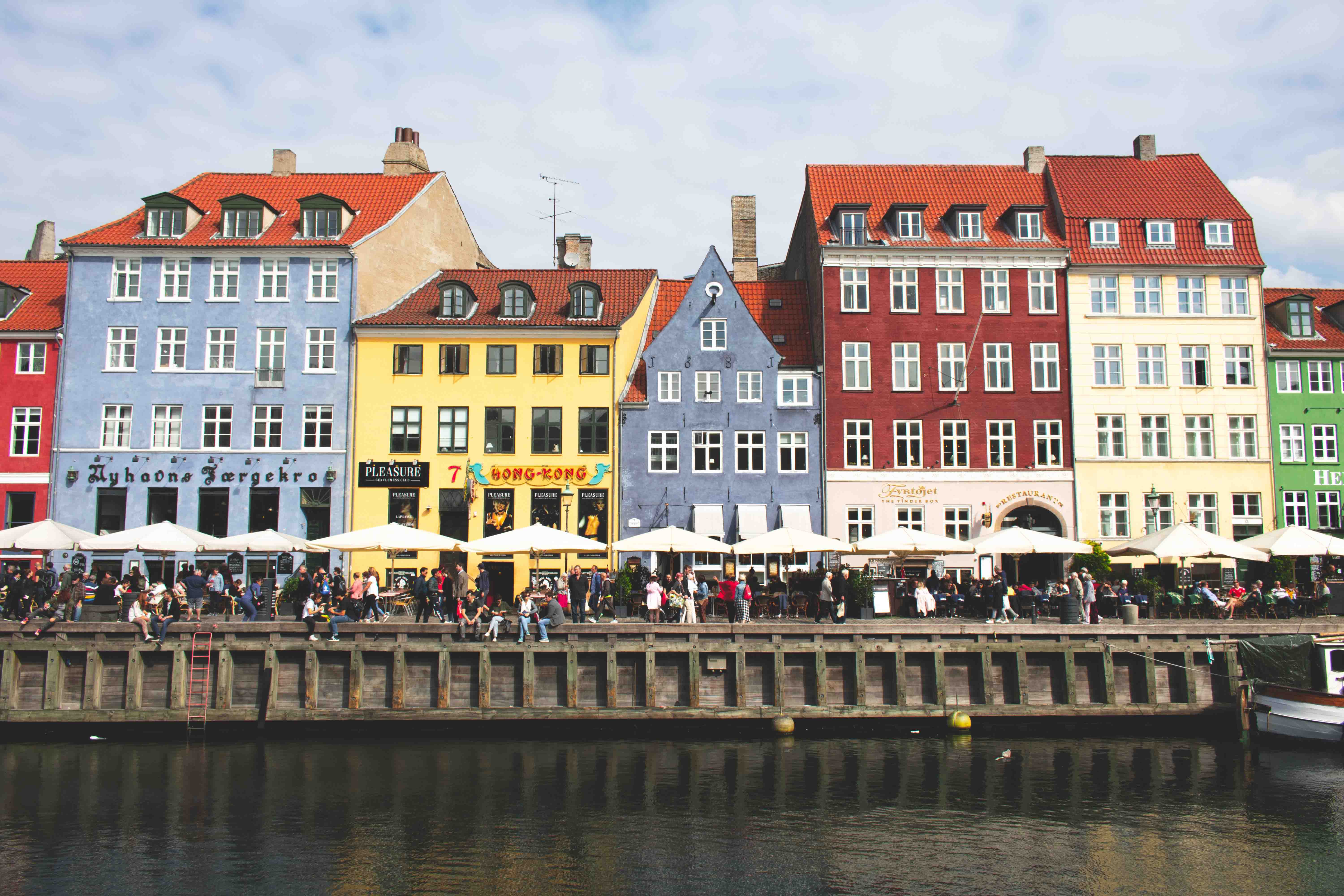Nyhavn sett fra vannet. Det er mange mennesker som går forbi de fargerike husene.