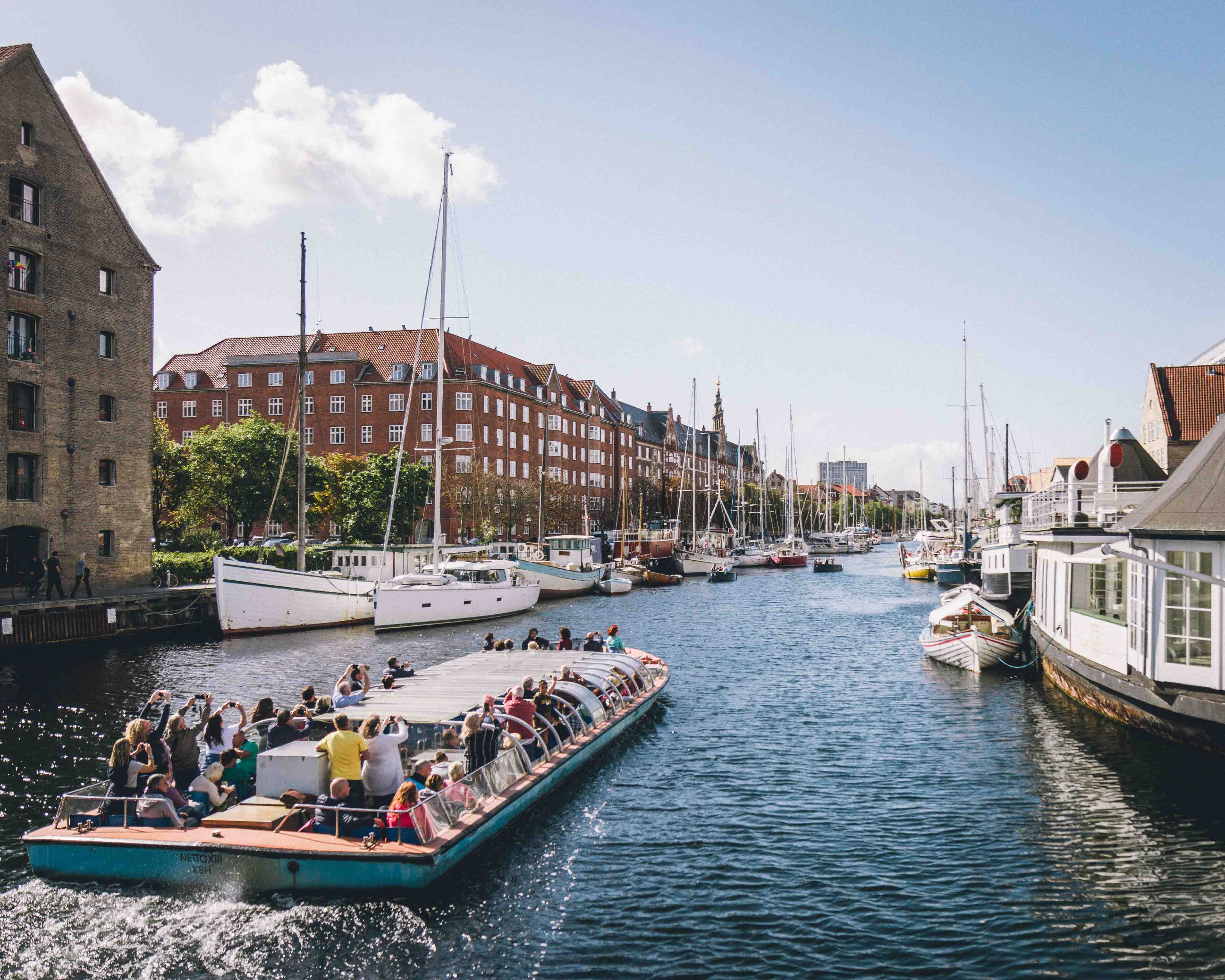 kanalbåt med turister som strekker hendene i været og tar bilder. DEt er en solfylt dag.