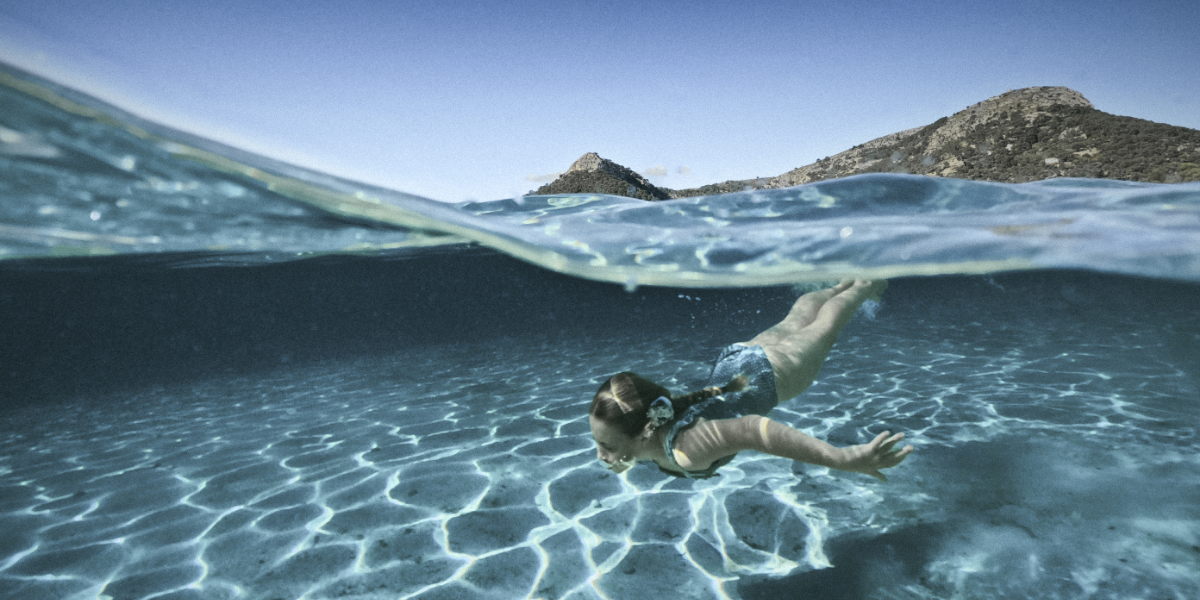 Girl diving under water with crystal clear ocean and mountains in background