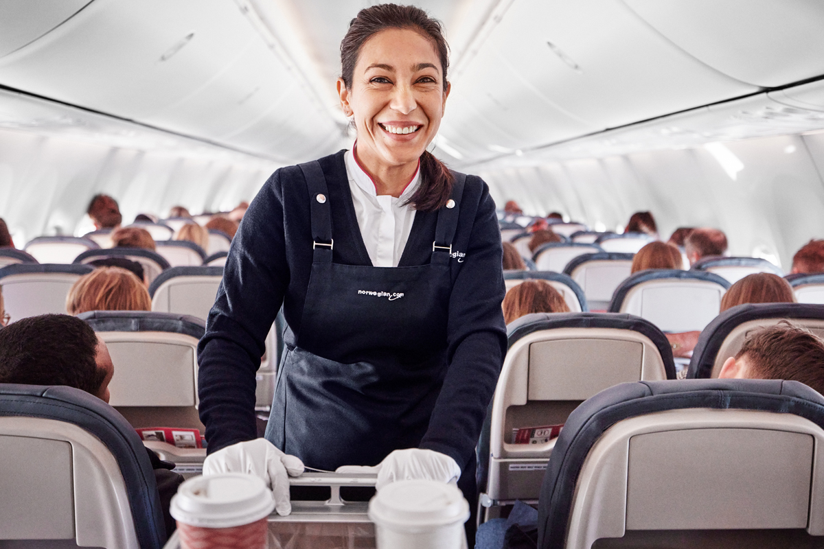 En kabinansatt står ved en serveringstralle inne i et fly.