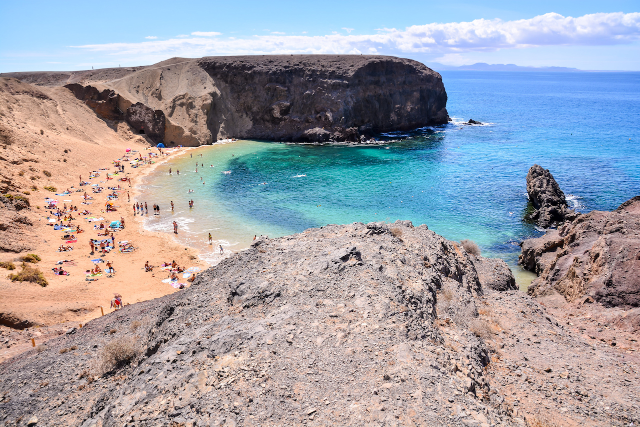 Vakker strand i Lanzarote med stort fjell på enden. Gul sand og mange mennesker