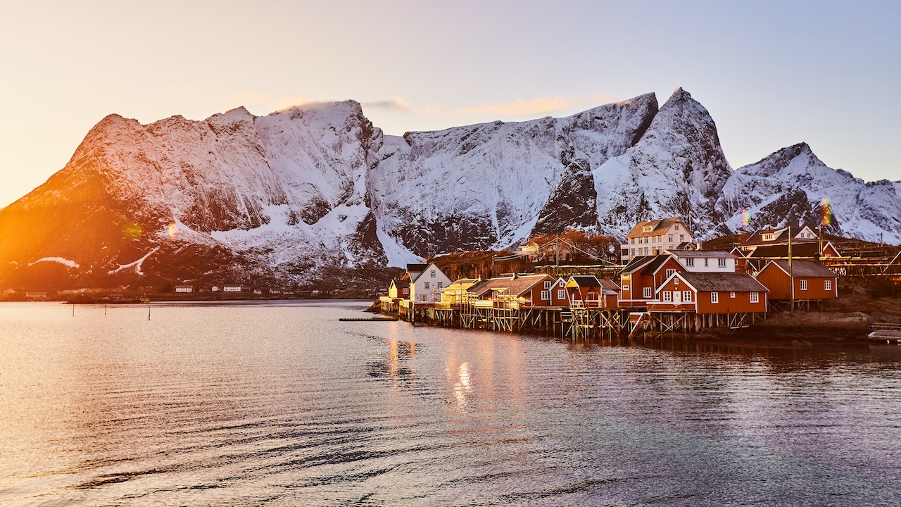 Solen går ned og kaster et orange lys over snødekte fjell og rorbuer