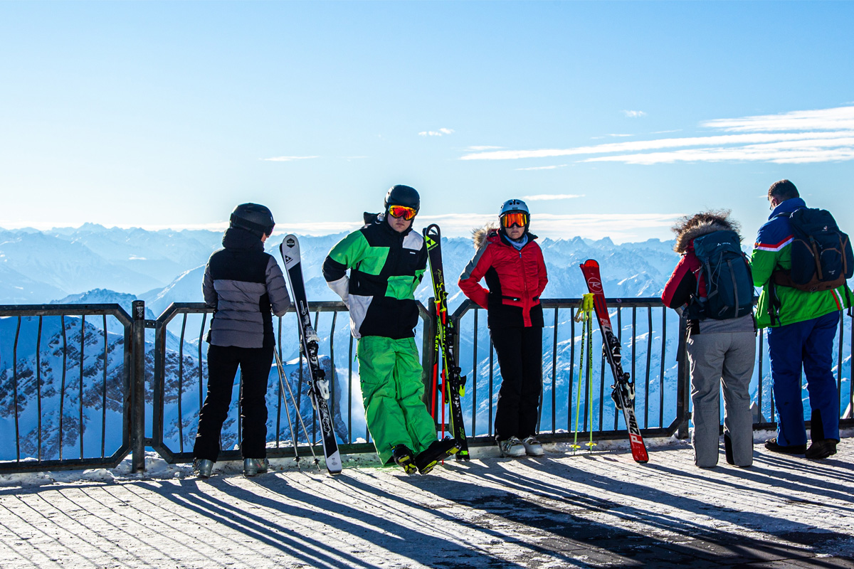 kvinner og menn i skidress foran et gjerde med utsikt over høye fjell