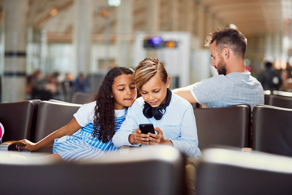 Søsken ser på samme mobiltelefon og smiler