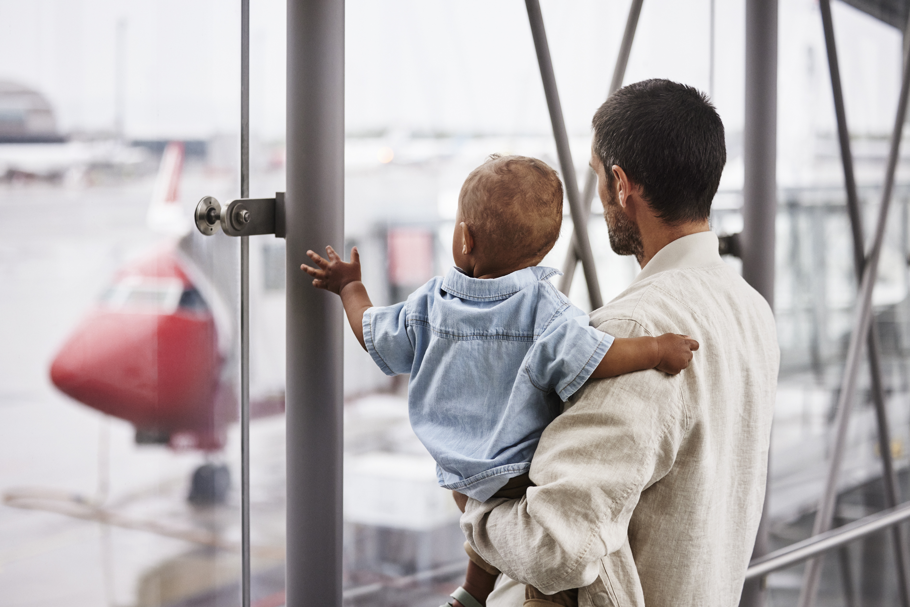 Far holder sin lille sønn og ser ut på flyet som står parkert ved gate