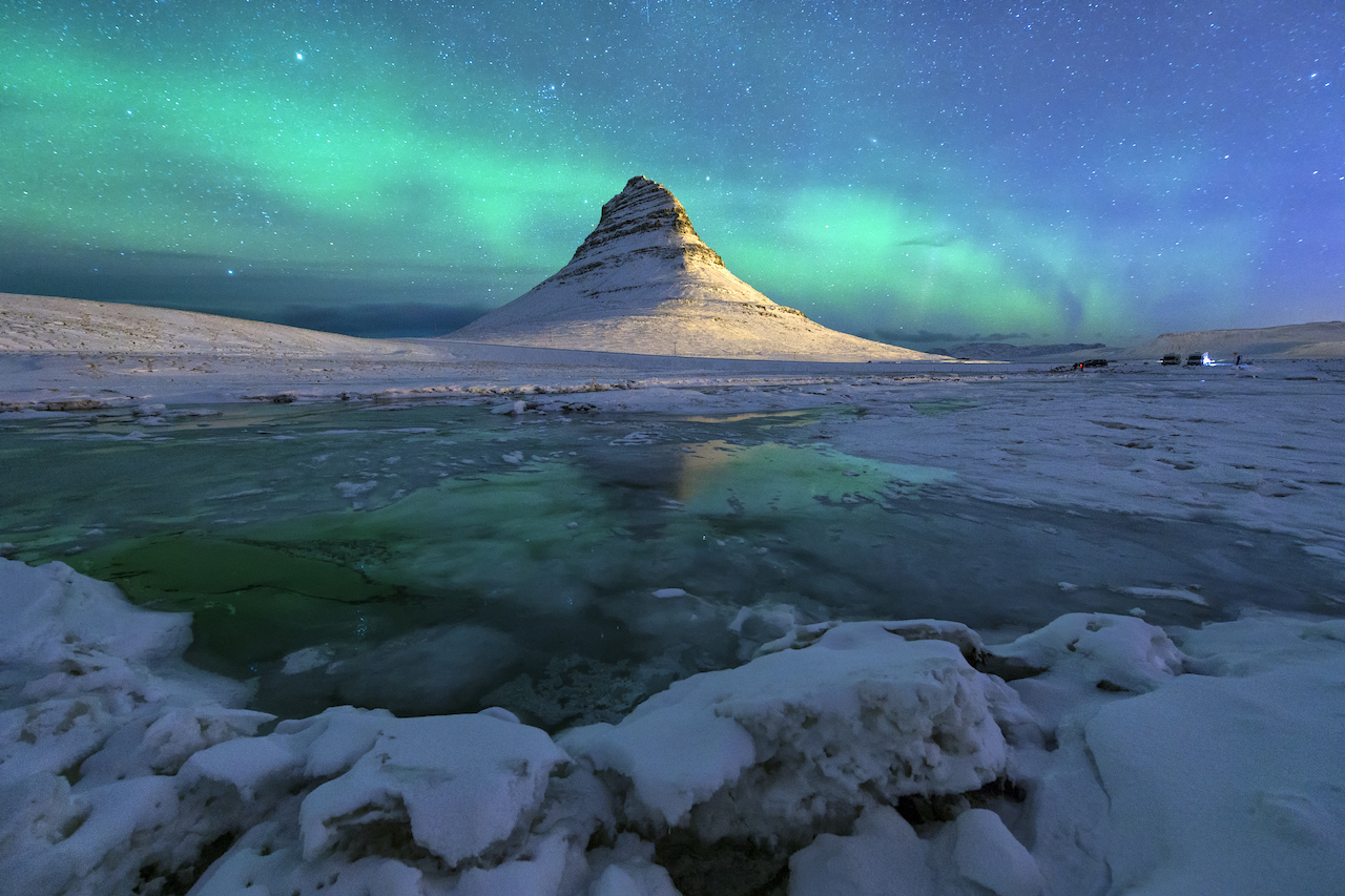 En spiss fjelltopp med sterkt nordlys dansene rundt