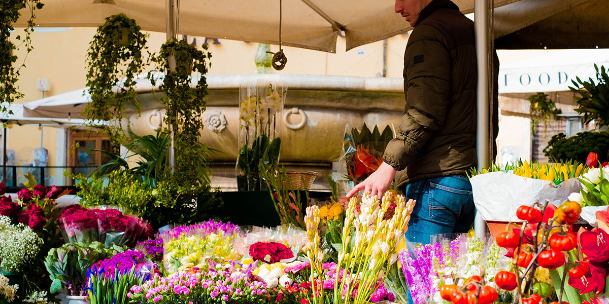En mann står ved et blomstermarked med vakre farger og parasoller