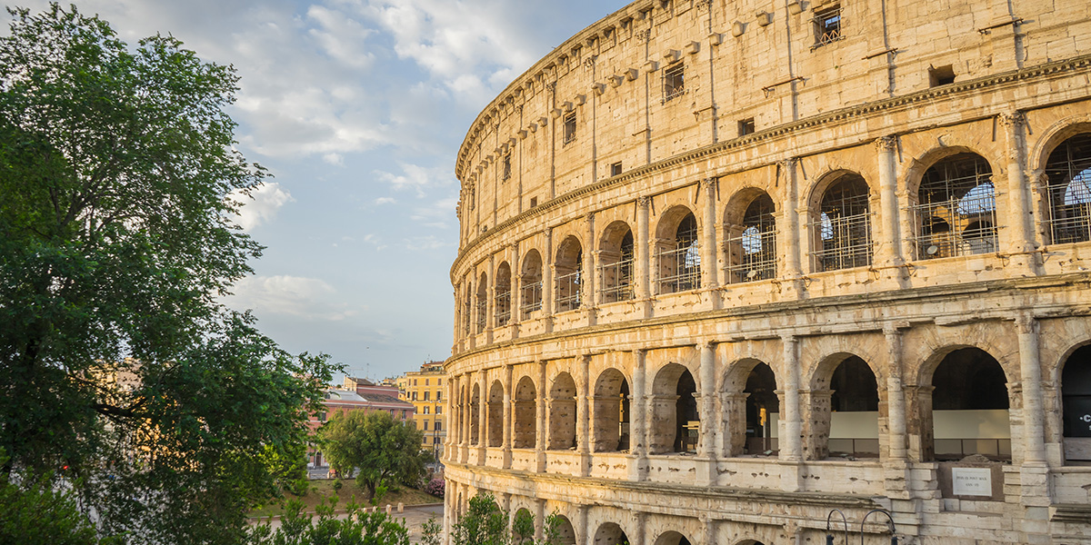 Litt av Colosseum i Roma sett utenfra, men noen trær i forgrunnen.