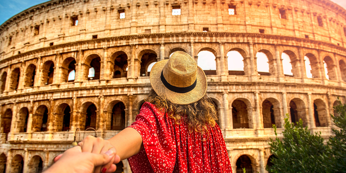En kvinne står rett foran og ser mot Colosseum i Roma, mens hun holder i en hånd.