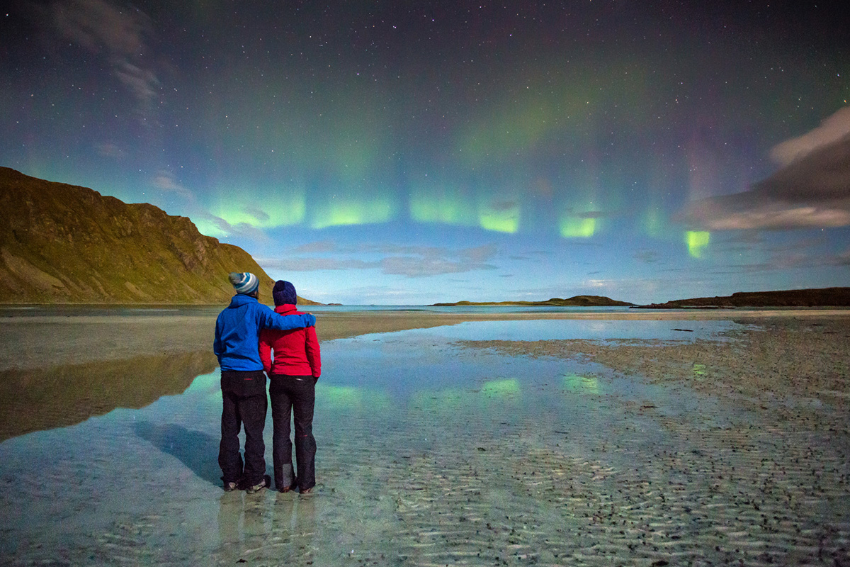 Et par ser på nordlyset på en strand