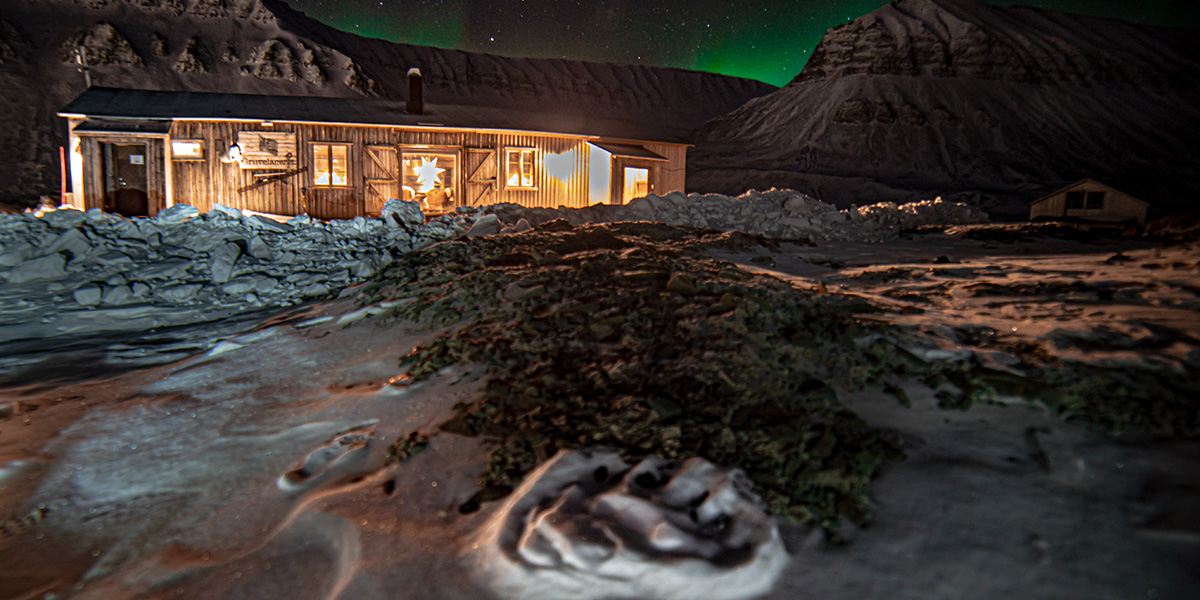 Utsyn over snøkledde fjell og en gammel tømmerkoie på Svalbard