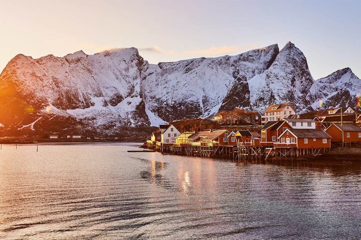 Fiskevær får lave solstråler mens store snødekte fjell stikker opp i bakgrunnen