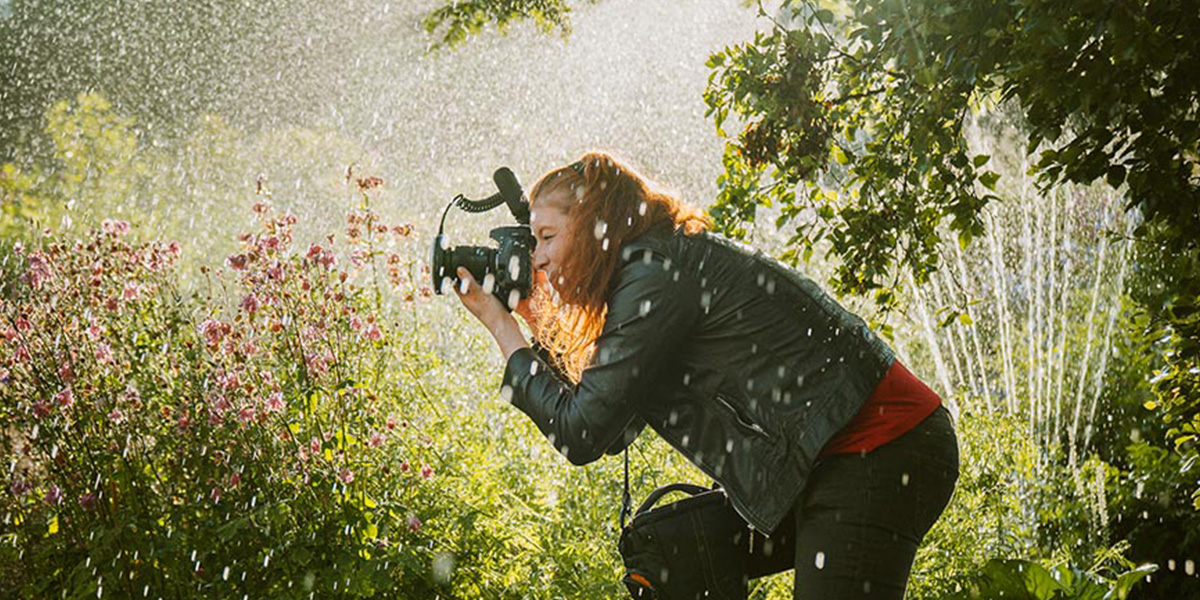 En kvinne står og fotograferer i et blomsterlandskap