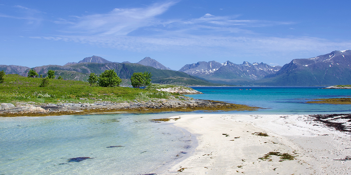 Arktisk hvit strand med fjell i bakgrunnen og turkist vann