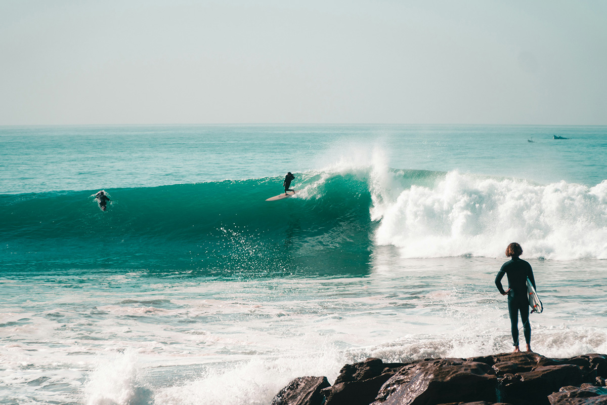 En bølge med surfere, der en surfer står på en klippe på land