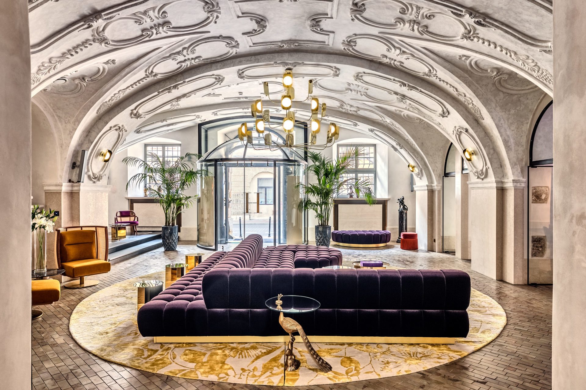 hotelllobby med buet hvitt tak, stor gullpendel lampe og mørk lilla designer sofa