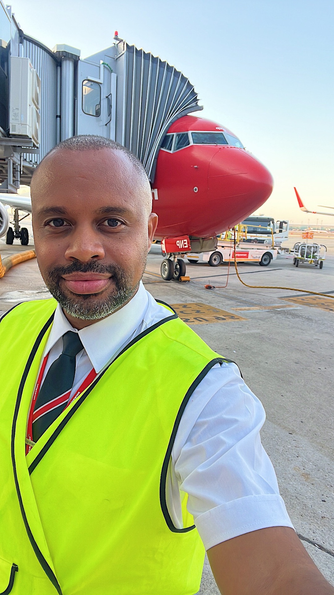 man takes a selfie in yellow reflective vest outside an aircraft